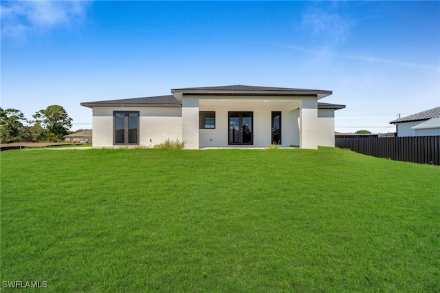 rear view of property featuring stucco siding, a yard, and fence