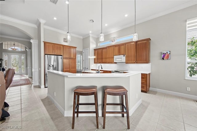 kitchen with stainless steel appliances, arched walkways, brown cabinetry, and decorative columns