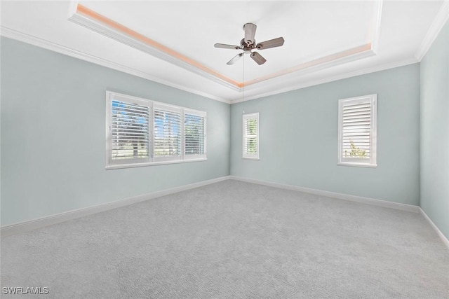 carpeted empty room with a ceiling fan, a tray ceiling, crown molding, and baseboards