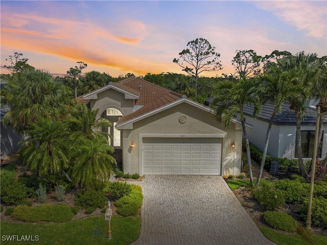 mediterranean / spanish home with a garage, a tiled roof, decorative driveway, and stucco siding