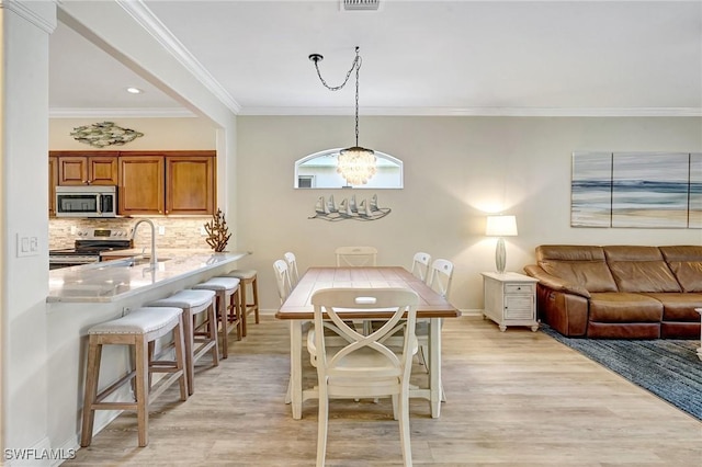 dining space with an inviting chandelier, light wood-style flooring, visible vents, and ornamental molding