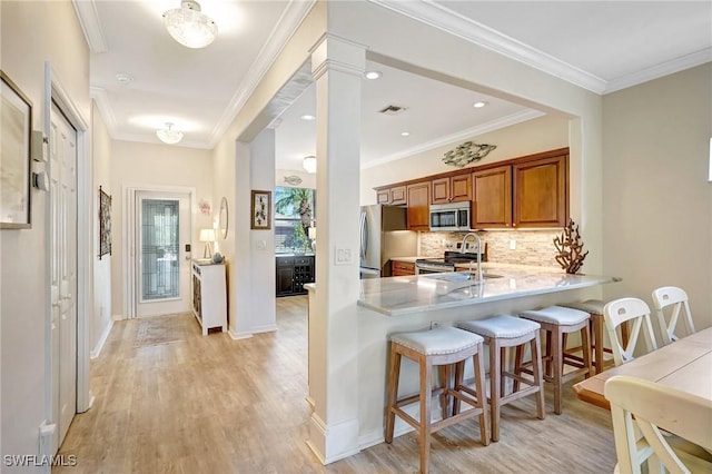 kitchen with appliances with stainless steel finishes, a breakfast bar, brown cabinets, light countertops, and a sink