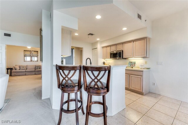 kitchen featuring light brown cabinetry, stainless steel microwave, and visible vents