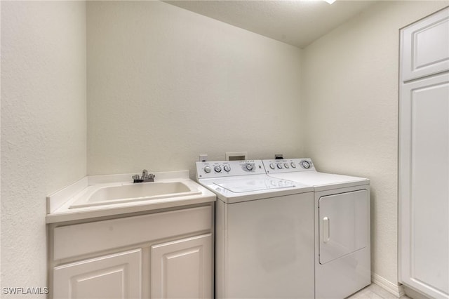 washroom featuring cabinet space, washer and clothes dryer, a sink, and a textured wall