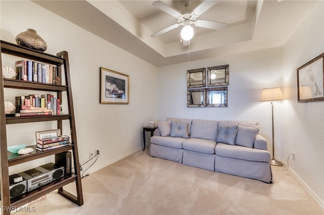 carpeted living area with ceiling fan, baseboards, and a raised ceiling