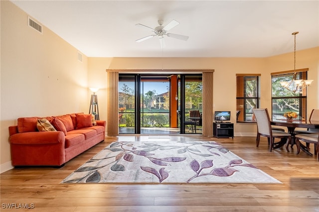 living area featuring a healthy amount of sunlight, visible vents, wood finished floors, and ceiling fan with notable chandelier