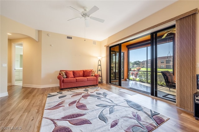 living area featuring arched walkways, visible vents, light wood-style floors, a ceiling fan, and baseboards