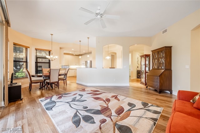 living room featuring light wood-type flooring, arched walkways, visible vents, and ceiling fan with notable chandelier