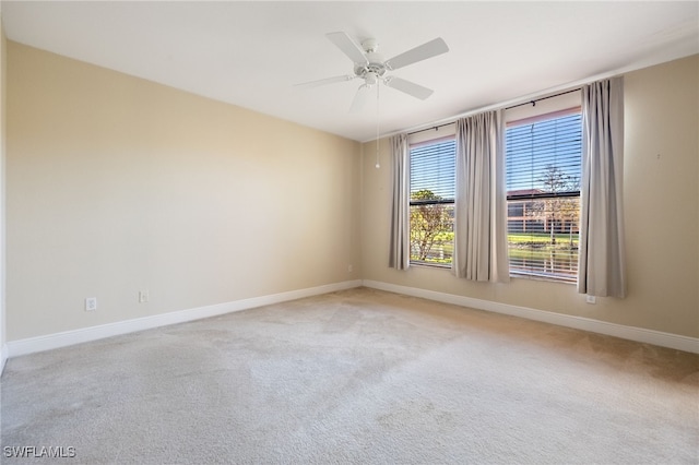 spare room featuring light carpet, a ceiling fan, and baseboards