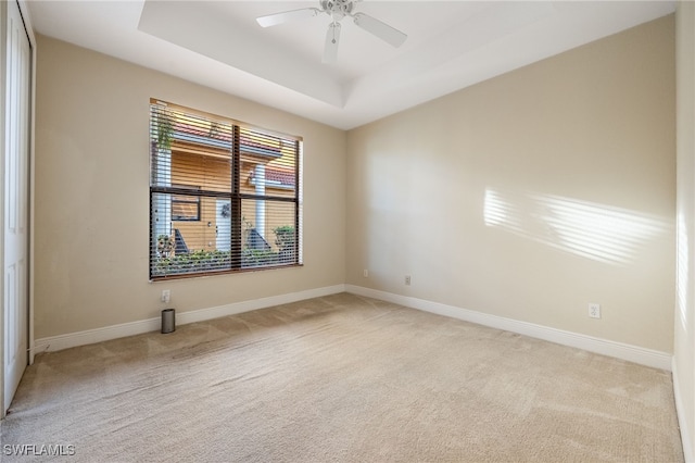 spare room featuring light carpet, a raised ceiling, a ceiling fan, and baseboards