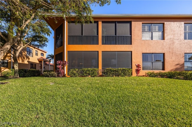 rear view of property featuring a lawn and stucco siding