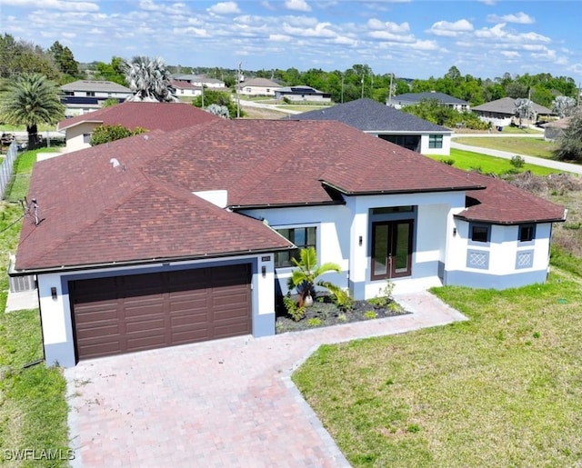 view of front of house with an attached garage, french doors, decorative driveway, stucco siding, and a front yard