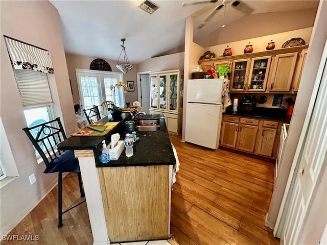 kitchen with a breakfast bar area, visible vents, brown cabinetry, freestanding refrigerator, and a sink