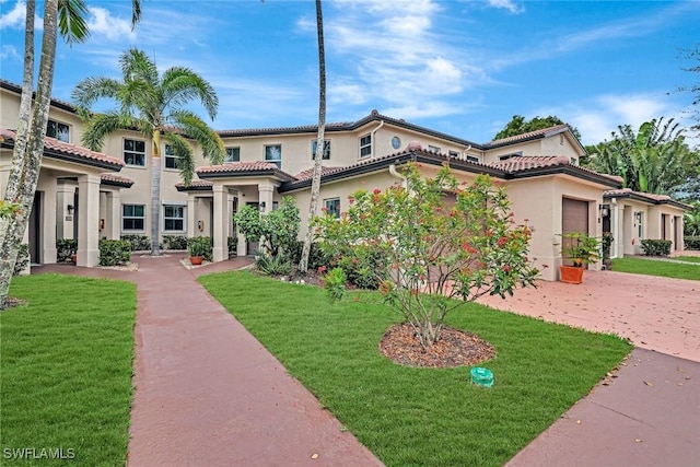 mediterranean / spanish home with a garage, a tiled roof, decorative driveway, stucco siding, and a front lawn