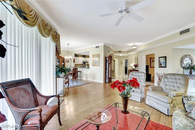 living room with light wood finished floors, visible vents, baseboards, ornamental molding, and ceiling fan with notable chandelier