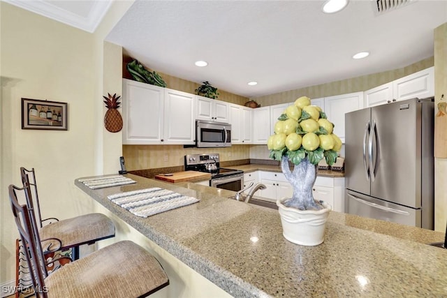 kitchen with visible vents, a breakfast bar, stainless steel appliances, white cabinetry, and a sink