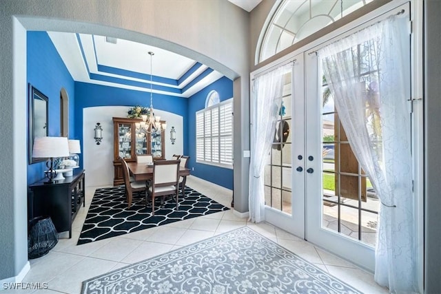 interior space featuring arched walkways, french doors, a raised ceiling, a chandelier, and baseboards