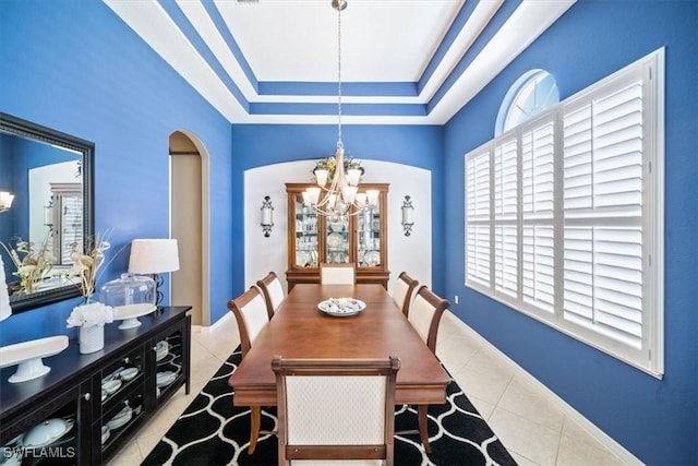 tiled dining area with baseboards, arched walkways, a chandelier, and a tray ceiling