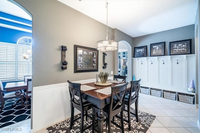 dining area with arched walkways, lofted ceiling, an inviting chandelier, wainscoting, and tile patterned floors