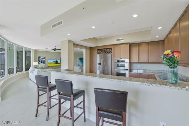 kitchen featuring stainless steel appliances, recessed lighting, visible vents, brown cabinetry, and a kitchen bar