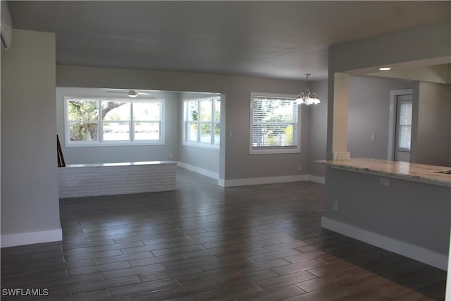 unfurnished room with ceiling fan with notable chandelier, an AC wall unit, dark wood-style flooring, and baseboards