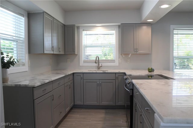 kitchen featuring light stone counters, stainless steel electric range, a sink, and gray cabinetry