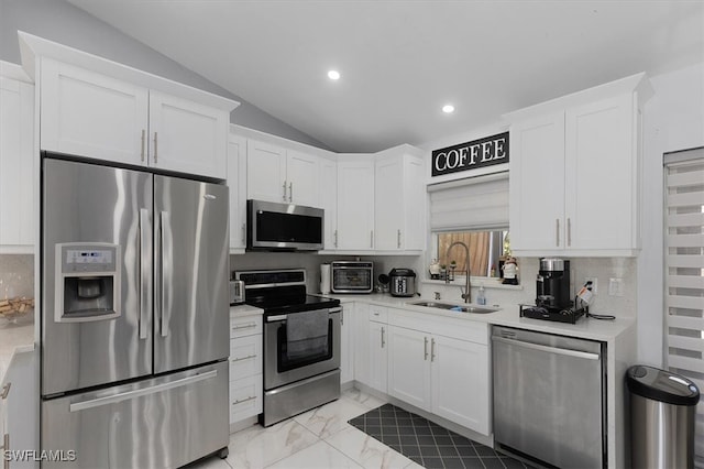 kitchen featuring stainless steel appliances, light countertops, white cabinets, vaulted ceiling, and a sink