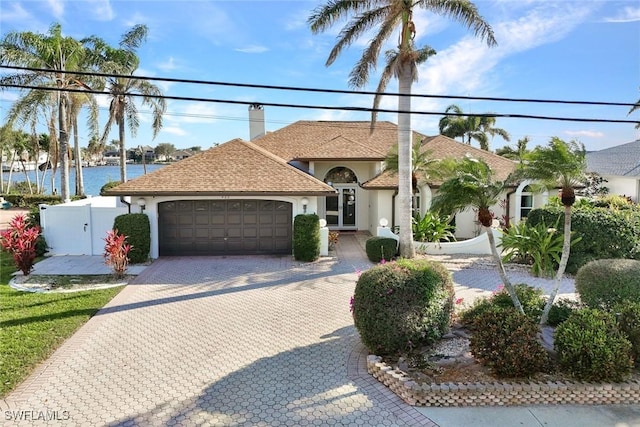 mediterranean / spanish-style house featuring a garage, fence, decorative driveway, stucco siding, and a chimney