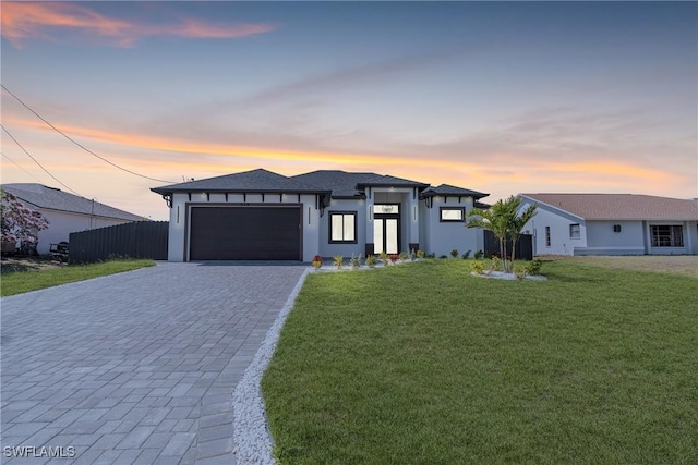 prairie-style house with a garage, fence, decorative driveway, a front yard, and stucco siding