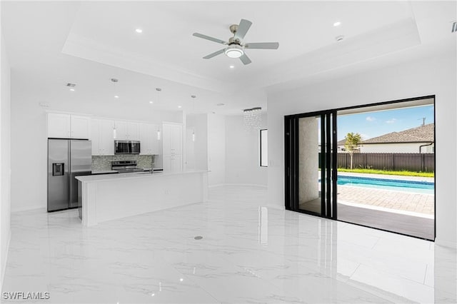 kitchen featuring a kitchen island with sink, stainless steel appliances, white cabinets, marble finish floor, and a raised ceiling