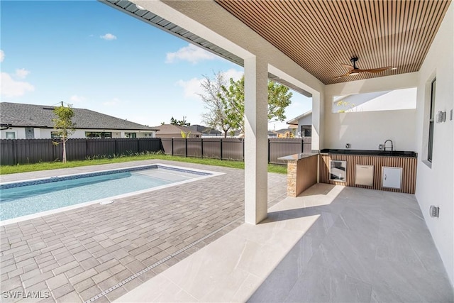 view of swimming pool with a fenced backyard, a fenced in pool, an outdoor kitchen, and a ceiling fan