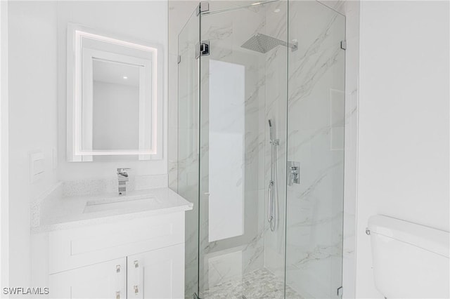 bathroom featuring toilet, a marble finish shower, and vanity