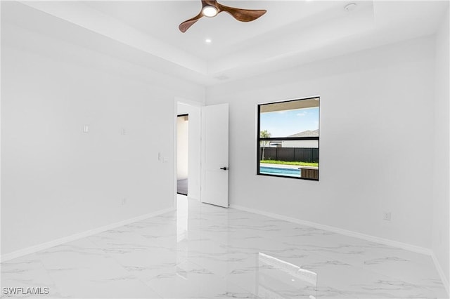 spare room with marble finish floor, a tray ceiling, recessed lighting, and baseboards