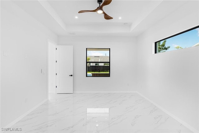 spare room with a tray ceiling, marble finish floor, and plenty of natural light