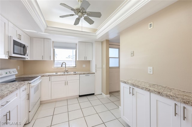 kitchen with white appliances, a raised ceiling, ornamental molding, white cabinetry, and a sink