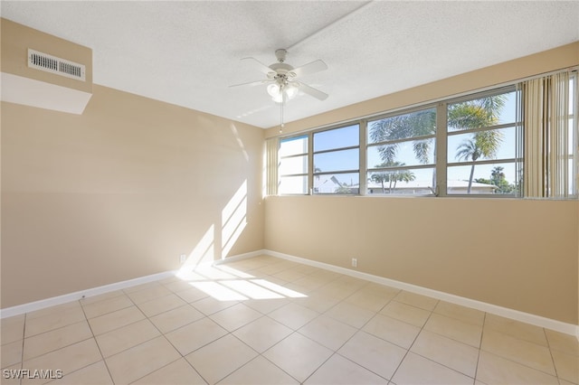 empty room with a textured ceiling, light tile patterned floors, visible vents, and baseboards