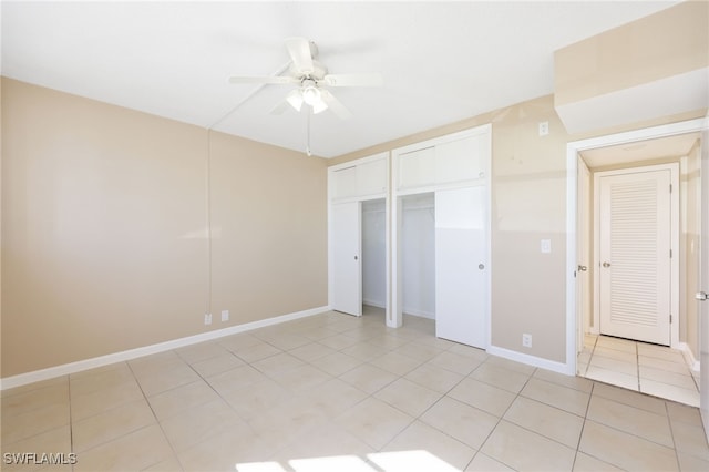 unfurnished bedroom with light tile patterned floors, baseboards, a ceiling fan, and multiple closets