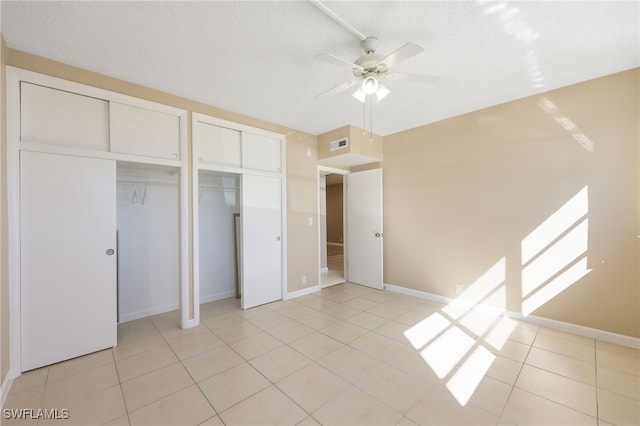 unfurnished bedroom featuring light tile patterned floors, visible vents, a textured ceiling, and two closets