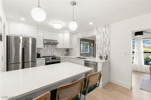 kitchen with a breakfast bar, stainless steel appliances, light countertops, under cabinet range hood, and a sink