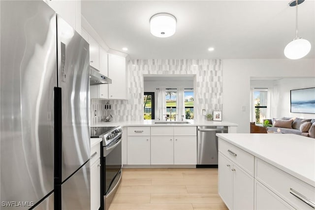 kitchen featuring white cabinets, appliances with stainless steel finishes, light countertops, under cabinet range hood, and a sink