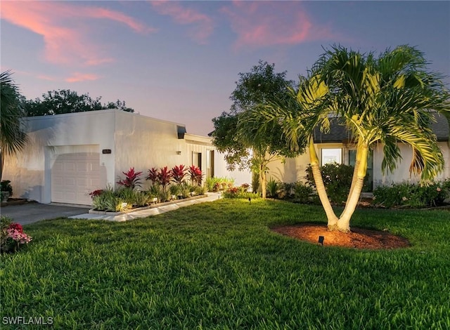 view of front of property featuring an attached garage, stucco siding, driveway, and a yard