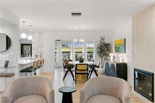 dining area featuring light wood-type flooring, baseboards, visible vents, and a glass covered fireplace