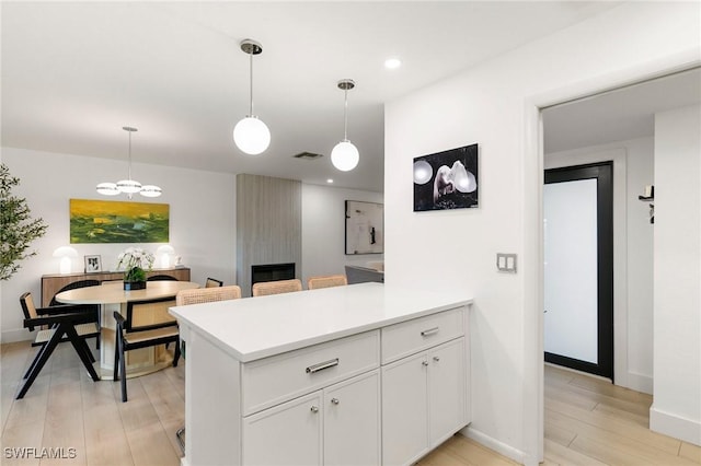 kitchen featuring light wood-style flooring, a peninsula, visible vents, white cabinets, and pendant lighting