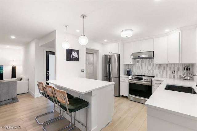 kitchen with decorative backsplash, a breakfast bar, stainless steel appliances, under cabinet range hood, and a sink