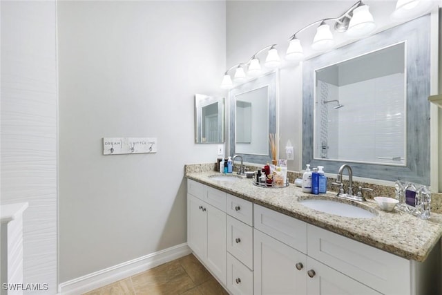 bathroom featuring double vanity, baseboards, a tile shower, and a sink