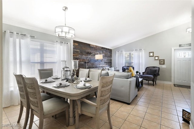 dining space with light tile patterned flooring, an accent wall, vaulted ceiling, ornamental molding, and an inviting chandelier