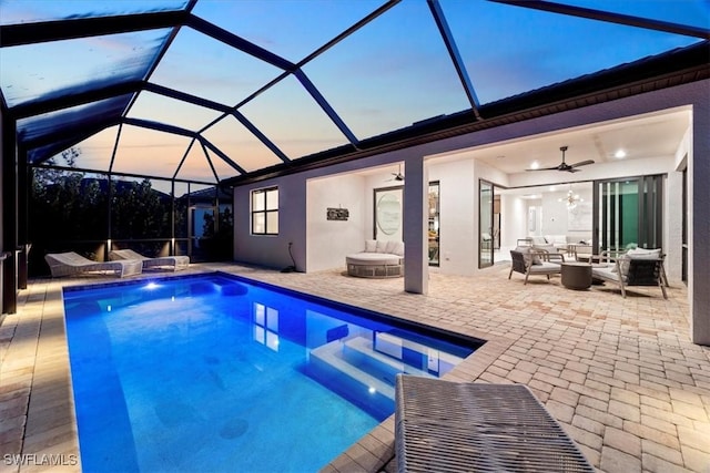 pool at dusk featuring a lanai, an outdoor hangout area, a patio, an outdoor pool, and a ceiling fan