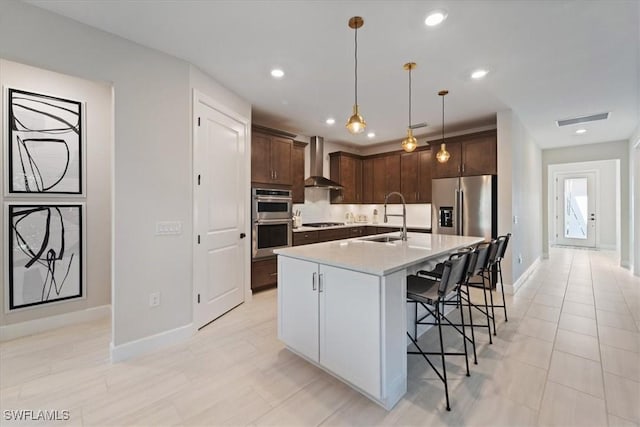 kitchen with a sink, wall chimney range hood, a kitchen breakfast bar, stainless steel appliances, and light countertops