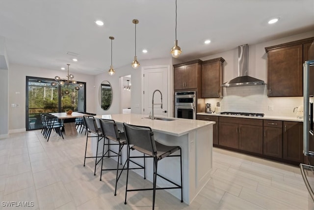 kitchen with double oven, a kitchen bar, gas stovetop, wall chimney exhaust hood, and a sink