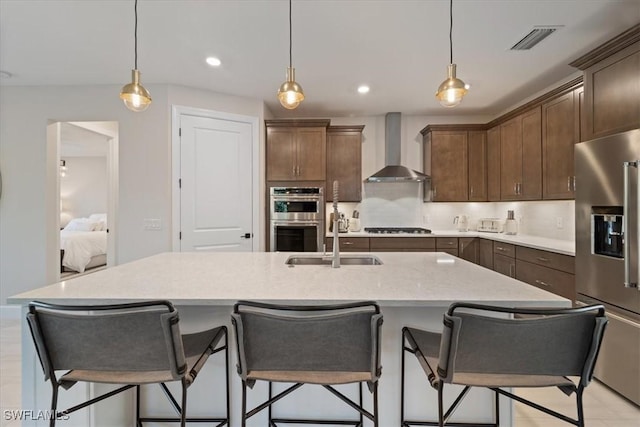 kitchen with visible vents, wall chimney range hood, light countertops, stainless steel appliances, and a sink